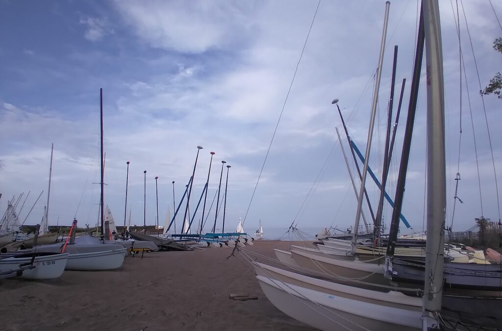 Sailboats lined up on a beach with Lake Michigan and some boats under sail in the distance